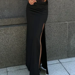 Mujer de pie, con parte superior de encaje, vistiendo una pollera maxi negra ajustada con un tajo alto en el muslo y frunces laterales.