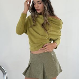 Skort de corderoy color oliva con pliegues, cierre lateral y detalle de botón, usado con un top verde y anillos dorados.
