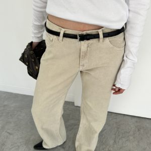 Mujer usando jean tiro bajo beige con remera blanca y cinturón negro, estilo relajado.