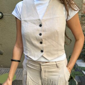 Chaleco sastrero corto (cropped) de lino color beige, con botones frontales y detalle de cinturón o abertura en la espalda. Ideal para usar solo o sobre básicos.