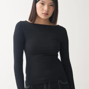 Modelo posando con la Remera Quell negra de Overwild, de manga larga y cuello bote, combinada con vincha de tachas.